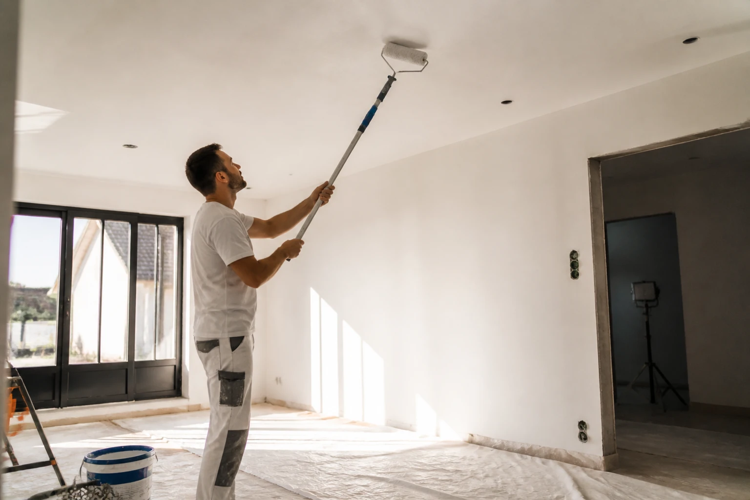 Homme appliquant de la peinture blanche mate sur un plafond avec un rouleau télescopique