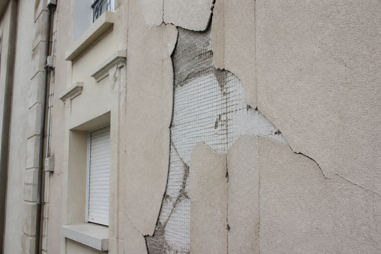 Façade de maison ancienne avec fissures et décollements sur l'enduit d'isolation thermique extérieure