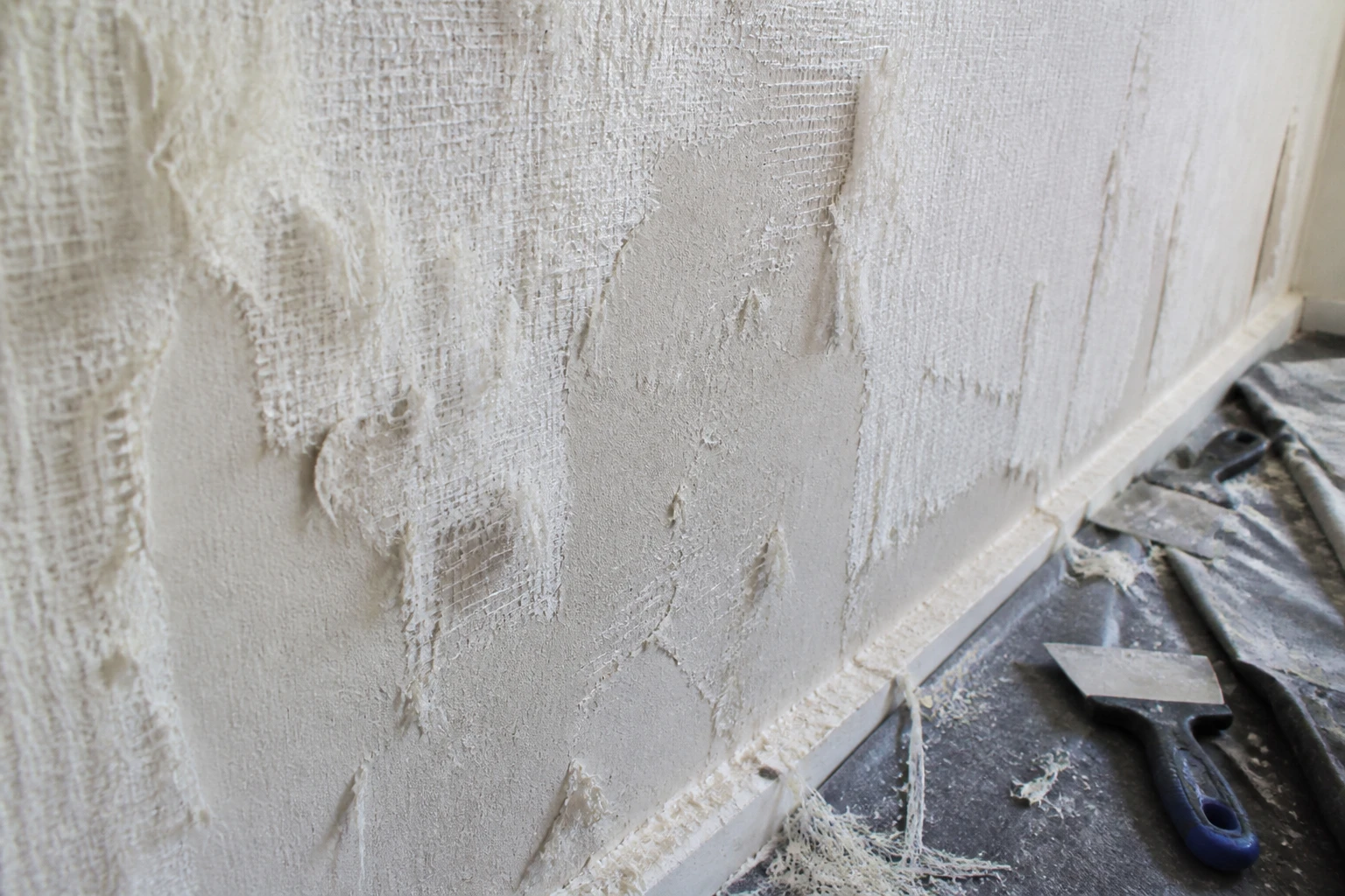 Dépose de toile de verre sur un mur ancien, filaments arrachés et plâtre dégradé visible
