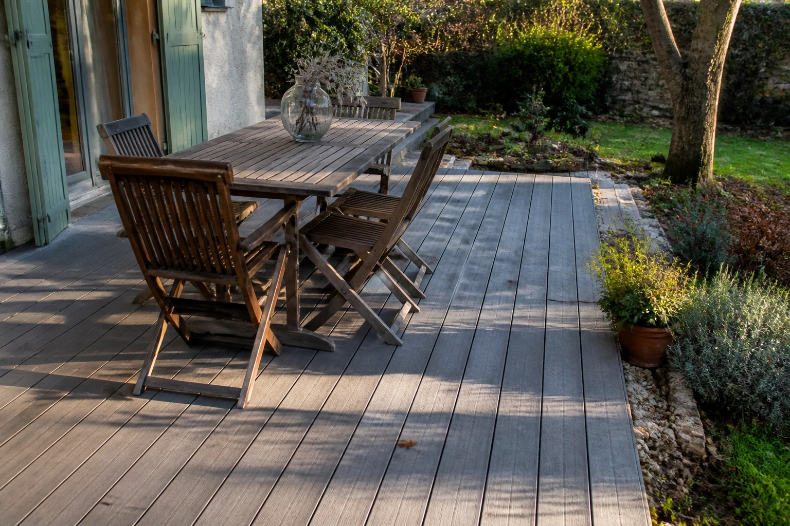 Terrasse en composite gris avec lames striées dans un jardin, lumière de fin de journée
